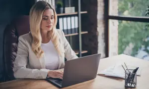 Kobieta w jasnej marynarce pracuje nad odpowiedzią na pozew przy laptopie w biurze.
