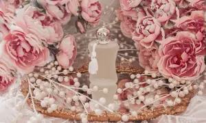 Flakonik Valaya Parfums de Marly otoczony różowymi różami i perłami, na złotym lustrzanym tacy.