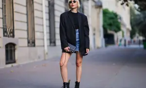 Kobieta w czarnym blazerze i jeansowej spódniczce nosi kultowe buty Dr. Martens, które mają bogatą historię.