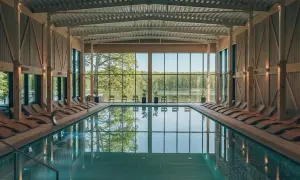 Basen w nowoczesnym spa z widokiem na jezioro i las. Drewniane leżaki i przeszklone ściany tworzą relaksującą atmosferę, idealną dla najlepszego spa w Polsce.