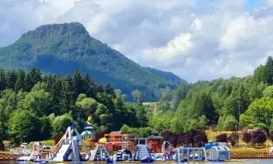 Kolorowy park wodny na wodzie przy górskim krajobrazie. **Radków zalew** zaprasza do zabawy na dmuchanych zjeżdżalniach i torach przeszkód.