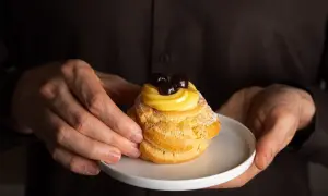 Mani che offrono una zeppola di San Giuseppe, un dolce con una ricca storia, guarnita con crema pasticcera e amarene.