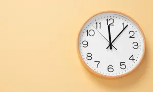 Reloj de pared blanco con marco de madera. Las manecillas marcan las 12:05. Ideal para aprender las horas en inglés, ejemplos.