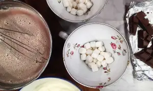 Förberedelser för en mysig stund med varm choklad. Vispad choklad i kastrull, marshmallows i skålar och chokladkakor redo att smältas.