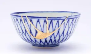 Cuenco de cerámica azul y blanco reparado con la técnica japonesa de kintsugi, resaltando las grietas con oro.