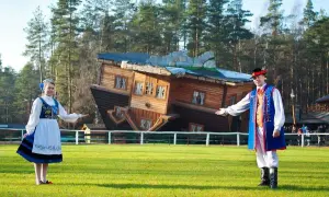 Para z ludźmi w strojach ludowych zaprasza do Domu do Góry Nogami, jednej z głównych atrakcji dla dzieci w Szymbarku.