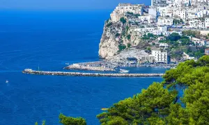 Rodi Garganico, Puglia: case bianche aggrappate alla scogliera, un porto con barche e il mare blu intenso.