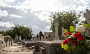 Nagrobek z krzyżami i kwiatami na tle pochmurnego nieba.
