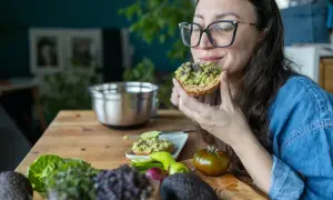 Frau genießt Avocado-Toast, ein gesunder Snack für das avocado abnehmen. Frische Zutaten liegen auf dem Tisch.
