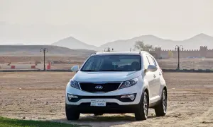 Białe Kia Sportage, jeden z popularnych modele kia, zaparkowany na pustynnym terenie z górami w tle.