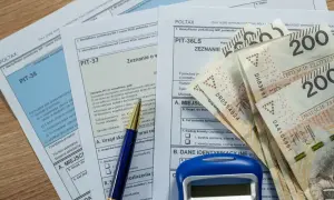 Formularze podatkowe PIT, długopis, kalkulator i banknoty 200 zł. Czas na rozliczenie roczne i zapłatę **czynszu** za mieszkanie.