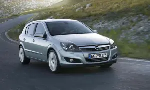 Srebrny Opel Astra 2005 na krętej drodze, otoczony zielonymi wzgórzami.