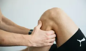 Fizjoterapeuta bada kolano pacjenta, dotykając jego mięśni.