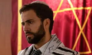 Ein Mann mit Bart und Kippa trägt einen Tallit. Im Hintergrund ist ein Davidstern auf rotem Stoff zu sehen. So sieht ein Jude aus.