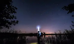 Ein Angler steht nachts im Wasser, beleuchtet von seiner Stirnlampe, unter einem sternenklaren Himmel.