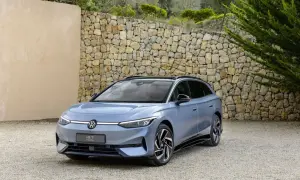 Niebieski Volkswagen ID.7 Tourer na żwirowym podjeździe, z kamiennym murem w tle.
