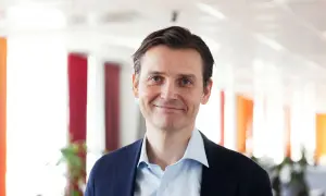 Peter Laurin, en man med blå ögon och mörkt hår, ler mot kameran i en mörkblå kavaj och ljusblå skjorta.