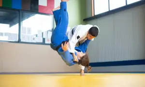 Dynamiczny rzut w judo, zawodniczka w niebieskim kimonie leci w powietrzu, grożąc nokautem w judo.
