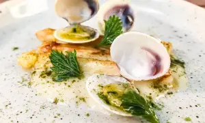 Delizioso piatto con pesce bianco, gamberi e **lupini di mare** in una salsa cremosa, guarnito con erbe fresche.