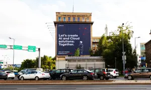 Na wielkiej reklamie z dominującymi **kolorami analogicznymi** – granatem i czerwienią – widnieje hasło "Let's create AI and Cloud solutions. Together.". W tle ruchliwa ulica z samochodami.