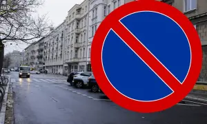 Znak B35 zakazu zatrzymywania się na mokrej ulicy z samochodami i kamienicami w tle.