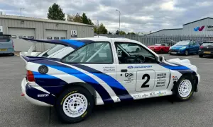 En vit rallybil Ford Escort Cosworth med blåa detaljer och nummer 2. Bilen står parkerad utomhus.