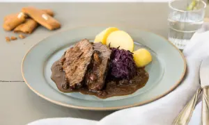 Ein Teller mit deftigem Braten, Rotkohl und Kartoffeln – ein schnelles Abendessen, das sättigt. Dazu ein Glas Wasser und ein paar Kekse.
