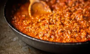 Herzhafte bolognese sauce köchelt in einer Pfanne, bereit für Pasta. Ein Holzlöffel rührt die fleischige Tomatensauce.