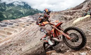 Motocyklista hard enduro na pomarańczowym motocyklu w kopalni odkrywkowej.