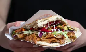 Kebab w bułce z mięsem, warzywami i sosami, trzymany w dłoniach.