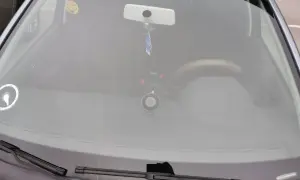 Bilens vindruta med en glad smiley-halsduk, backspegel och en dashcam. Perfekt för en stenskott besiktning.