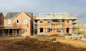 Cantiere edile con case in costruzione, una quasi finita e l'altra con impalcature. Il terreno è fangoso, con macchinari da scavo. Un esempio di **case abusive** in fase di realizzazione.