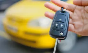 Kluczyk samochodowy z pilotem i wbudowanym immobilizerem w dłoni, na tle żółtego auta.