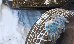 Rękawice leżą na oponie pokrytej śniegiem, gotowe do zmiany opon na zimowe.