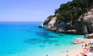 Rajska plaża Cala Goloritze z turkusową wodą, skalistym klifem i łukiem skalnym. Ludzie kąpią się i odpoczywają na piasku.