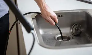 Mann führt ein Rohr in den Spülbeckenabfluss ein, um ihn zu reinigen.