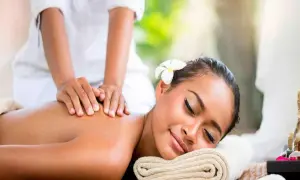 Mujer disfrutando un masaje relajante en un ritual spa. Una flor adorna su cabello mientras manos expertas alivian la tensión de su espalda.