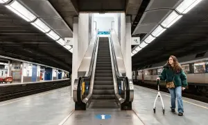Kobieta z chodzikiem na peronie kolejowym obok schodów ruchomych.