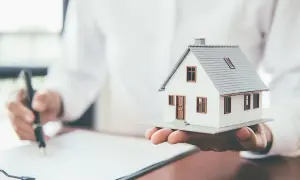 Osoba podpisuje dokumenty, trzymając w dłoni model domu. To może być wniosek o wykreślenie hipoteki.