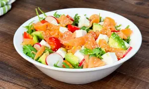 Insalata fresca con salmone affumicato, avocado, pomodorini, ravanelli e cubetti di formaggio, cosparsa di semi di sesamo.