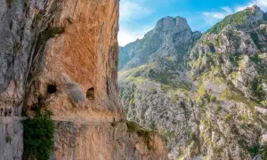Senderos tallados en roca, con personas caminando. El inicio y fin de la ruta del Cares se pierden entre imponentes montañas verdes y cielos azules.