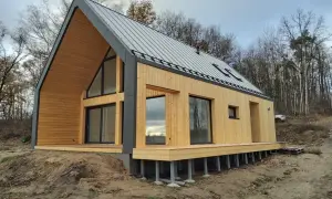 Nowoczesny dom modułowy z drewnianą elewacją i dużymi oknami, otoczony lasem. Zastanawiasz się, ile kosztuje dom modułowy?