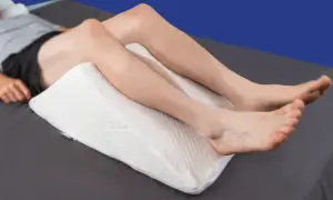 A person is resting with a white wedge pillow under their knees, providing comfort for sleeping with pillow under knees.