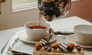 Tetera floral vierte té rojo en taza blanca. Bandeja con dulces y otra taza, perfecto para la hora del té en Inglaterra.