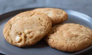 Tre gyllene white chocolate chip cookies på en mörkgrå tallrik, redo att avnjutas.