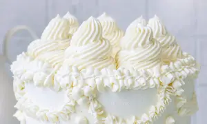 Ein weißer Kuchen, üppig dekoriert mit amerikanischer Buttercreme in kunstvollen Tupfen und Rüschen.