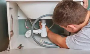 Mężczyzna naprawia syfon pod umywalką. Jak dobry **zdun**, dba o szczelność instalacji.