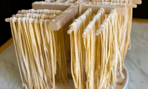 Świeży, domowy makaron w tagliatelle wiszący na drewnianym stojaku do suszenia.