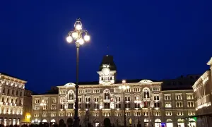Piazza Unità d'Italia a Trieste, illuminata di sera. Edifici storici e lampioni creano un'atmosfera magica.