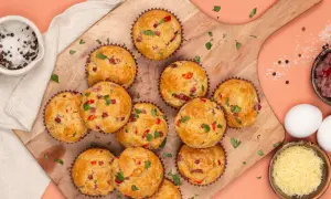 Herzhafte Pizza Muffins mit Speck und Paprika, garniert mit Petersilie. Daneben Zutaten wie Eier, Käse und Gewürze.